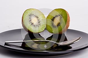 Kiwis next to each other on a black plate in front of a teaspoon