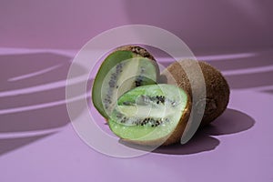 Kiwis sliced open on pink background with tropical leaf shadows