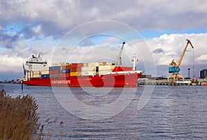 Klaipeda, Lithuania - 02 06 21: huge red cargo container ship on winter Curonian lagoon in front of terminal industrial