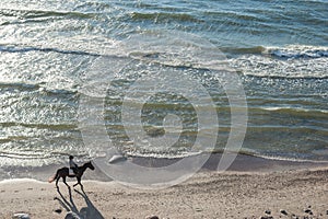 KLAIPEDA, LITHUANIA - SEPTEMBER 28, 2012: Woman is riding with horse on the beach of Baltic Sea