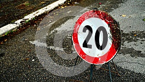 20km speed limit construction site sign, damaged by time on asphalt seen photo