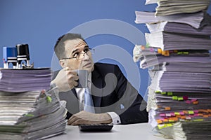 Knackered office employee looks frightened at high stack of documents