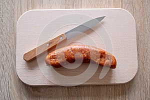 A knackwurst or sausage  on a platter with a knife to cut photo