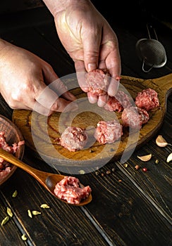 Kneading minced meat by the cook hands to prepare meatballs. Work environment with vegetables and spices on the kitchen table