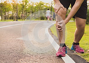 Knee Injuries. Young sport man holding knee with his hands in pain after suffering muscle injury during a running workout at park