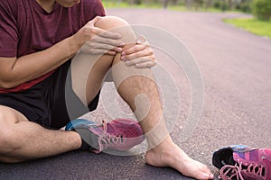 Knee Injuries. Young sport man holding knee with his hands in pain after suffering muscle injury during a running workout at park