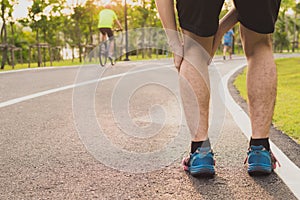 Knee Injuries. Young sport man holding knee with his hands in pain after suffering muscle injury during a running workout at park