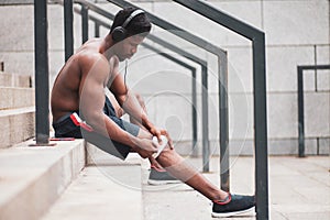 Knee injury concept, afro american guy bandaging his leg with a bandage, a man injured his knee in training