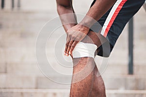 Knee injury concept, afro american guy bandaging his leg with a bandage, a man injured his knee in training