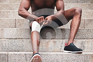 Knee injury concept, afro american guy bandaging his leg with a bandage, a man injured his knee in training