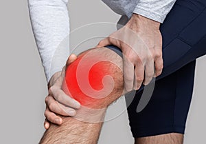 Knee injury or inflammation. Man in sportswear presses his hands to knee highlighted in red