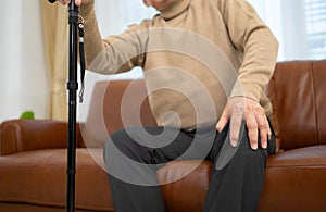 senior guy sits on a sofa with a walking stick in his living room at home