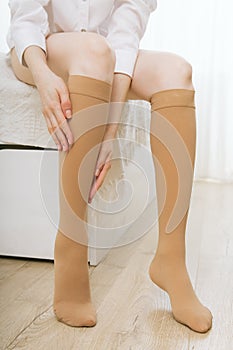 Knee socks or socks. Beige compression stockings on a woman in a white room. Girl putting on stockings at home