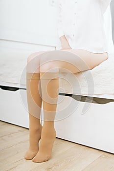 Knee socks or socks. Beige compression stockings on a woman in a white room. Girl putting on stockings at home