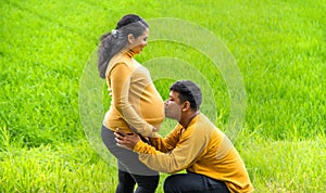 Kneel down and kiss her pregnant belly, countryside nature background