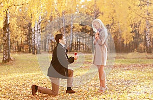 Kneeled man proposing ring to a woman in autumn