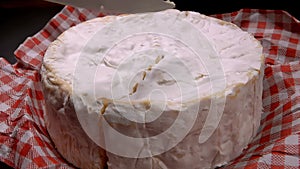 Knife carves a sector of round Camembert cheese