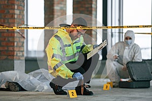 Knife clue. Detectives are collecting evidence in a crime scene near dead body. Forensic specialists are making expertise