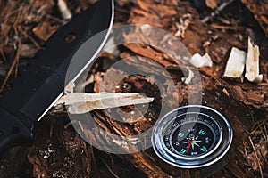 Knife and compass lie on ground in forest. Concept of survival in a wild forest area.