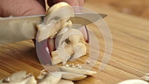 Knife cuts champignons into small pieces on a board