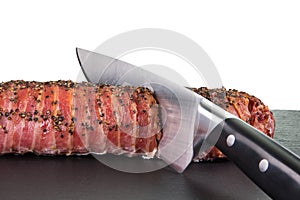 Knife is cutting a big portion of roast pork on a dark slate wit