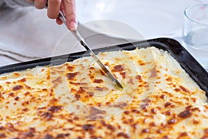 Knife cutting cannelloni with bÃ©chamel sauce in a pan