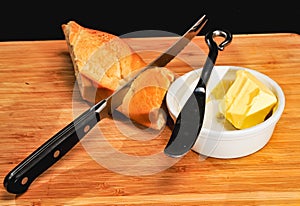 Knife cutting French baguette and ramekin with butter and knife