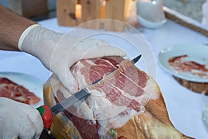Knife cutting serrano man hand slicing of italian dry cured ham prosciutto