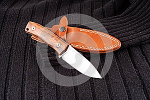 Knife with a fixed blade. Knife and leather sheath. Knife against the background of a knitted black sweater. photo