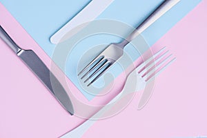 Knife and fork creative flat lay on soft pink and blue background