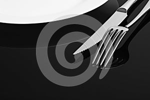 Knife, fork and empty plate on the black background