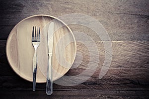 Knife and fork on wood plate placed on a wooden table - still life.