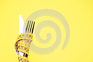 Knife and fork wrapped in a measure tape on a yellow background