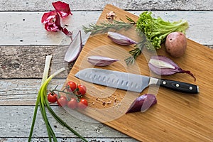 Knife with healthy food - vegetables, onion, salad, tomatoes, potato placed on a cutting board with wood background top view