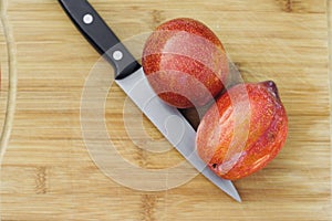 A Knife Next to Two Amigo Pluots on a Wood Chopping Board