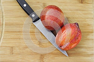 A Knife Next to Two Amigo Pluots on a Wood Chopping Board photo