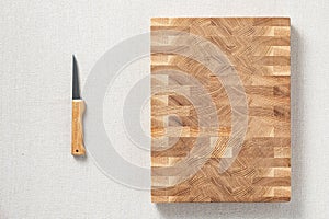 A knife and an oak spliced â€‹â€‹wooden cutting board are on burlap. The cross-section of the oak plank has a mosaic texture. Back