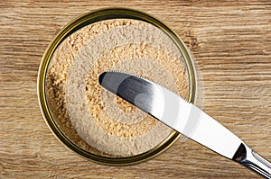 Knife on opened jar with sterilized cod caviar on wooden table. Top view