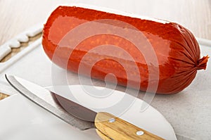 Knife on plate, sausage on cutting board on wooden table