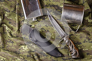 Knife, scabbard, metal flask and mug on camouflage fabric