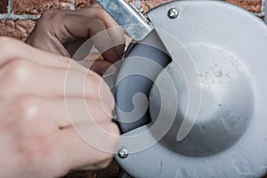 Knife sharpener and hand with blade on wooden table, closeup