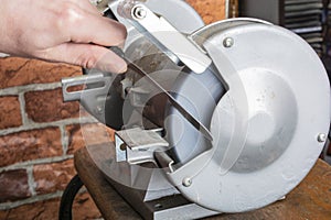 Knife sharpener and hand with blade on wooden table, closeup