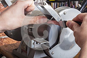 Knife sharpener and hand with blade on wooden table, closeup