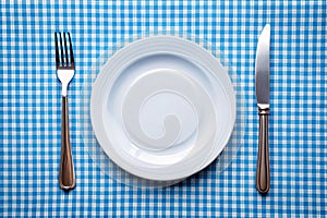 Knife, white plate and fork on blue checked tablecloth