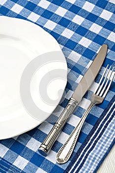 Knife, white plate, and fork on blue checked tablecloth