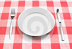 Knife, white plate and fork on checked tablecloth
