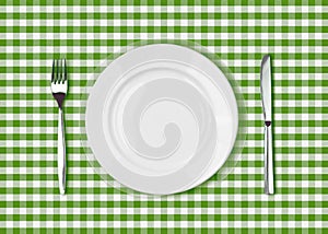 Knife, white plate and fork on green picnic table cloth