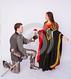 Knight in armor gives a young woman in a medieval dress a rose flower. Fantasy illustration for a book novel