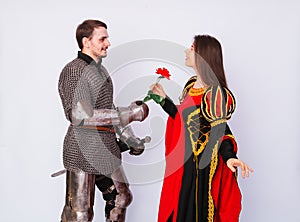 Knight in armor gives a young woman in a medieval dress a rose flower. Fantasy illustration for a book novel