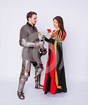 Knight in armor gives a young woman in a medieval dress a rose flower. Fantasy illustration for a book novel